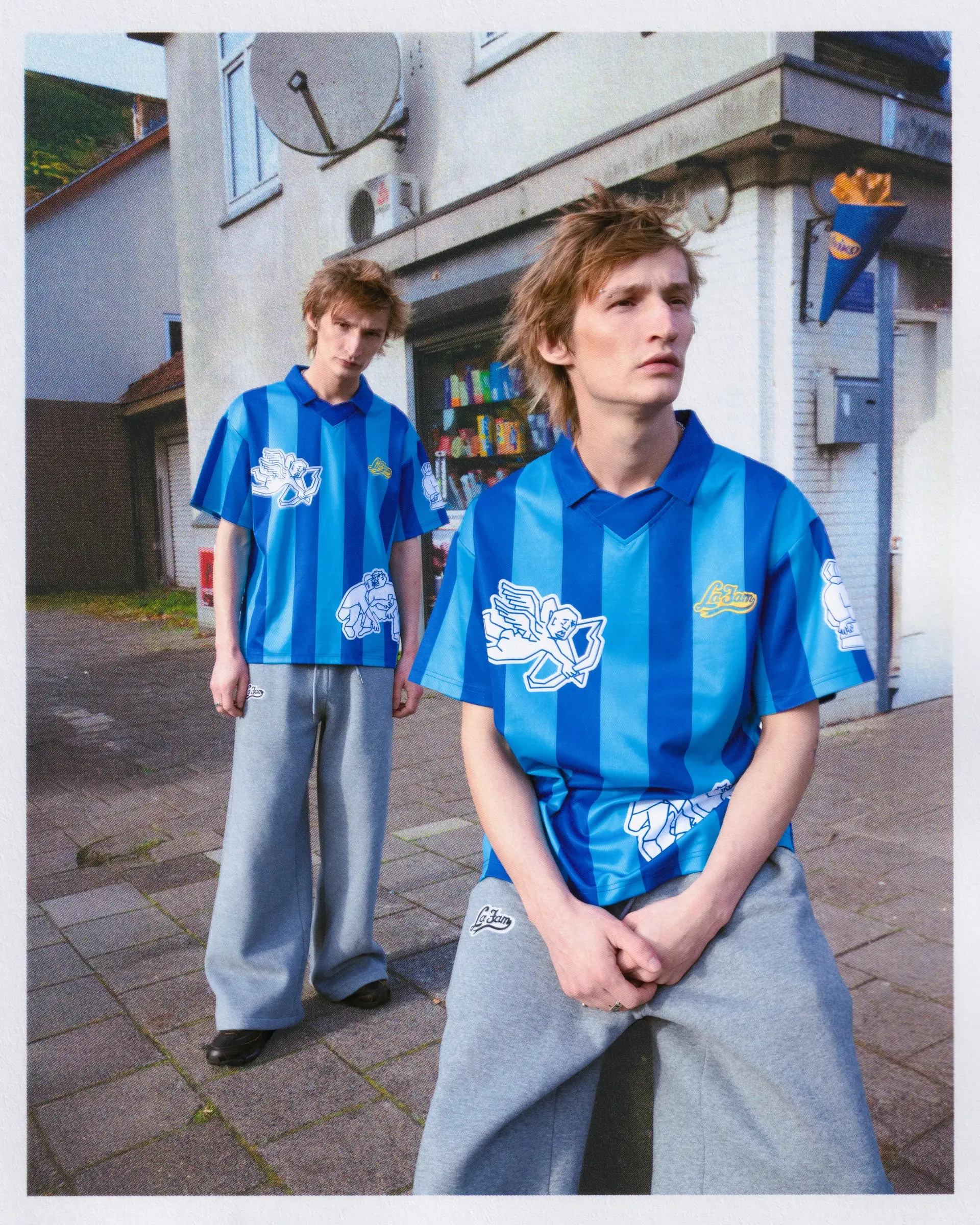 Two people in blue striped football shirts and grey trousers on a street corner.