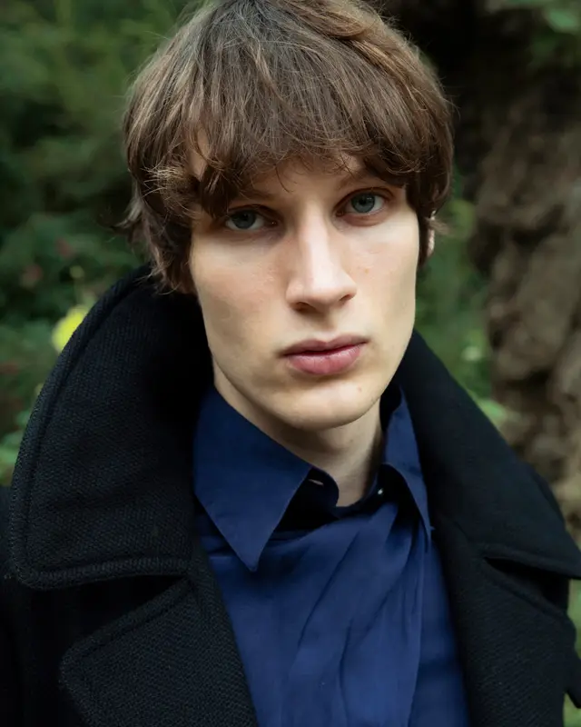 Close portrait of a young man in a black coat and navy shirt.