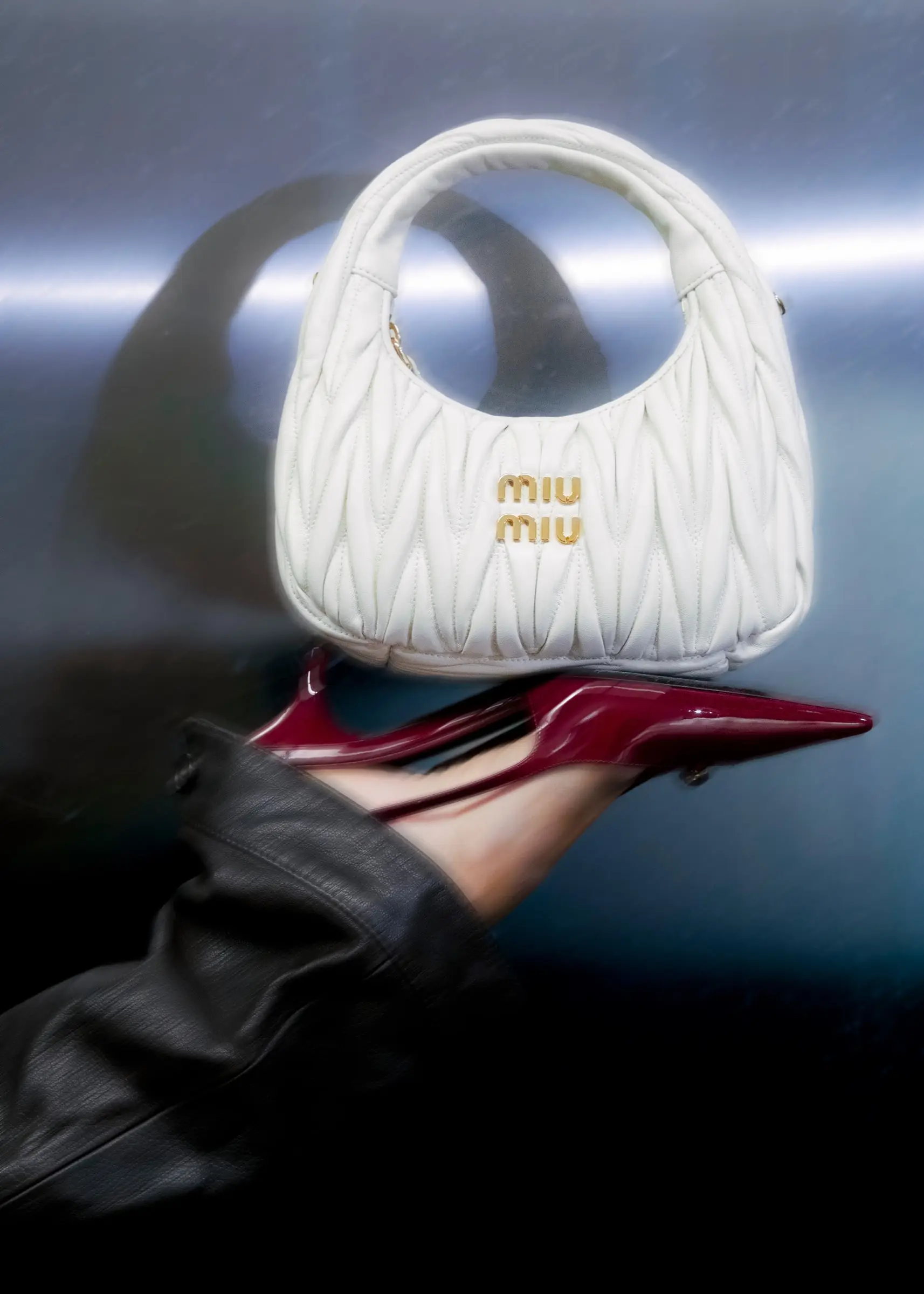 Close-up of a white quilted handbag and a burgundy pointed shoe held by a hand in a leather sleeve.