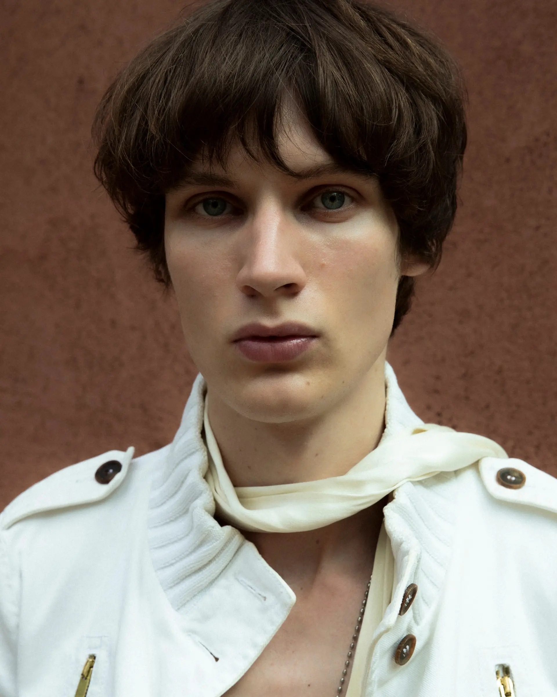 Close portrait of a young man with a white scarf against a brown wall.